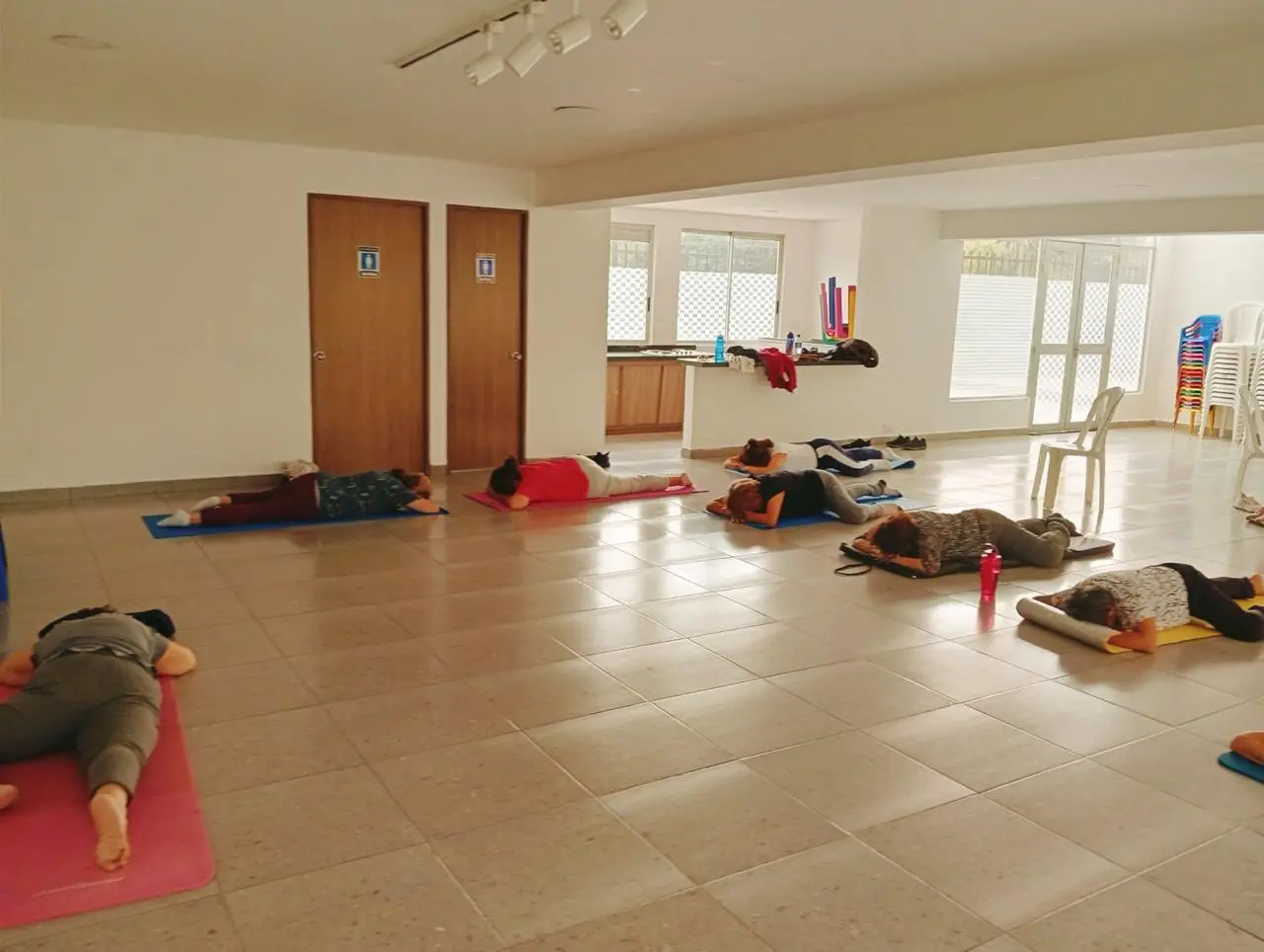 Grupo de personas realizando una actividad corporal sobre esterillas en una sala luminosa
